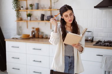 Evde kitap okurken elinde kalem tutan esmer kadın, kişisel gelişim kavramı.
