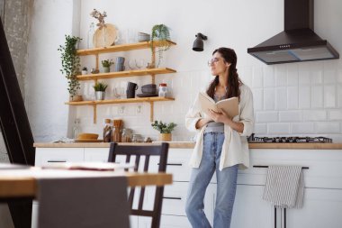 Rahat esmer kadın, elinde kitapla mutfakta dikilirken gözlerini kaçırıyor. 