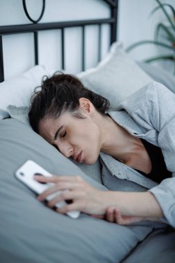 Evde yatakta yatarken akıllı telefonu tutan depresyondaki kadın, duygusal stres konsepti.