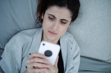 Üzgün bir kadının evde yatarken bulanık akıllı telefon kullanması, akıl hastalığı konsepti.