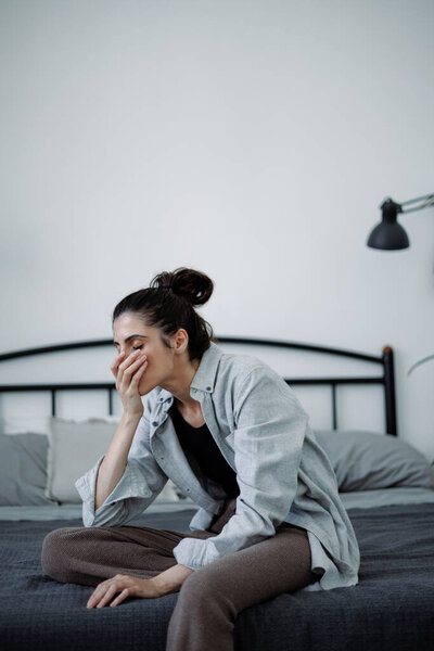 Overwhelmed brunette woman covering mouth while sitting on bed at home
