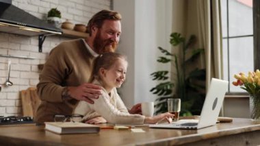 Gülümseyen baba ve kahveyi kucaklayan kız evde dizüstü bilgisayar kullanıyor.