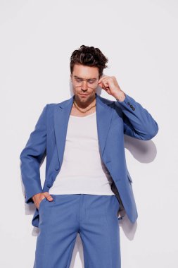 Mavi takım elbiseli esmer adam ve gri arkaplanda poz veren beyaz atlet. 