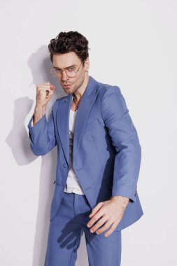 Kolsuz tişörtlü şık bir adam ve gri arka plandaki kameraya el kol hareketi yapıyor.