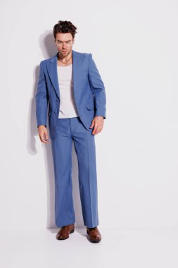 Gri arka planda mavi takım elbiseli, kendine güvenen ve şık bir adam.