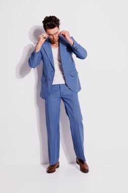 Gözlüklü, kolsuz tişörtlü ve gri üzerine mavi takım elbiseli moda bir adam. 