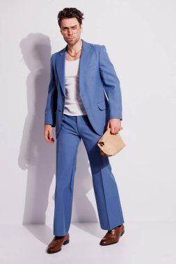 Mavi takım elbiseli şık bir adam Gri renkli kağıt torba tutuyor.