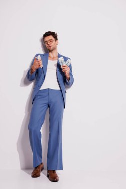 Mavi takım elbiseli, gözlüklü, gri duvarın yanında dolar sayan şık bir adam.