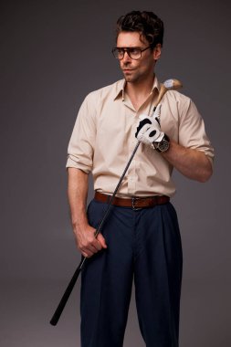 İyi giyimli, gözlüklü ve eldiven takan esmer bir adam. Golf sopası, gri moda konseptiyle izole edilmiş. 