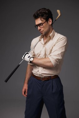 Gözlüklü şık oyuncu ve eldiven tutan golf sopası gri moda konseptinde izole edilmiş. 