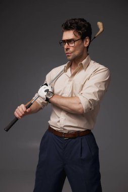 Şık giyinmiş esmer bir adam ve elinde golf sopası tutan gözlüklü gri bir adam. 