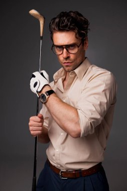 Klasik tişörtlü ve gözlüklü şık esmer adam, elinde golf sopası olan gri renkli bir adam. 