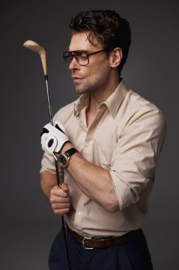 Klasik giyinmiş şık bir adam ve elinde golf sopası tutan gözlüklü gri bir adam. 