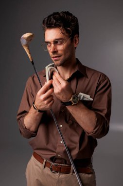 Gözlüklü şık ve şık bir adam. Üzerinde para ve golf sopası olan bir gömlek. 