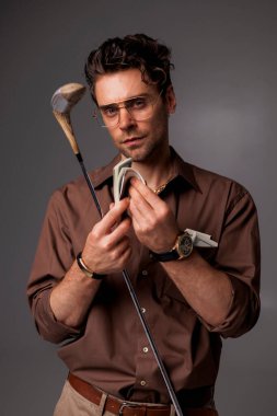 Zarif ve zarif bir adam. Kahverengi gömlekli. Elinde dolar ve golf sopası var. 