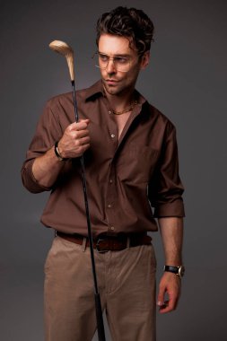 Gri yolda golf sopası tutan kendine güvenen ve yakışıklı esmer adam. 