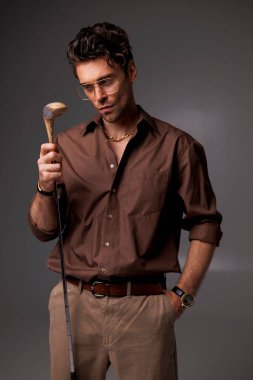 Gözlüklü ve tişörtlü şık bir adam. Golf sopası, gri moda konseptiyle izole edilmiş.