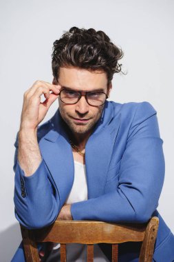 Mavi takım elbiseli, altın zincirli, gri gözlüklü, kendine güvenen ve şık bir adam. 