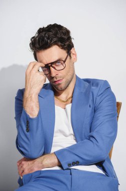 Gözlüklü, mavi takım elbiseli ve gri sandalyede oturan şık esmer adam.