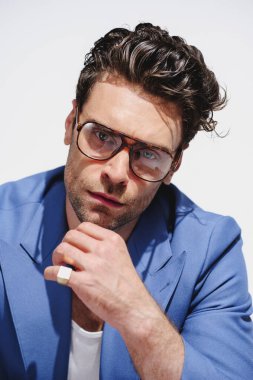 Gözlüklü, mavi ceketli, kendine güvenen ve şık bir adamın portresi gri renkli kameraya bakıyor. 