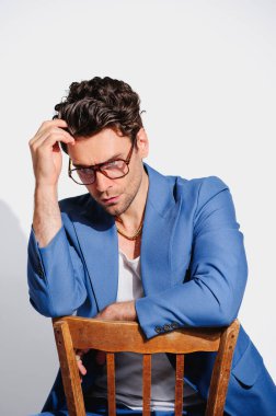 Mavi ceketli ve gözlüklü şık bir adam gri sandalyede oturuyor. 90 'ların moda konsepti 