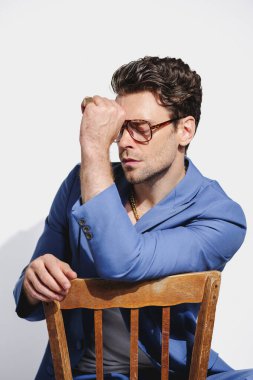 Modaya uygun gözlüklü ve mavi ceketli bir adam gri, 90 'ların konseptinde sandalyede oturuyor.