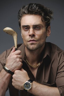 Lüks aksesuarlı şık bir adamın portresi ve gri üzerine izole edilmiş golf sopası tutan bir gömlek. 