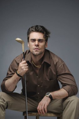 İyi giyimli, klasik kıyafetli ve gözlüklü bir adam. Golf sopası tutuyordu.
