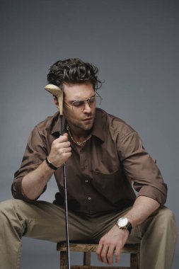 Pahalı kol saati ve tişörtü olan şık bir adam, elinde golf sopası tutuyordu.