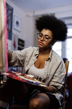 Atölyede bulanık tuvalin yanında boya paleti tutan Afrikalı Amerikalı sanatçı 