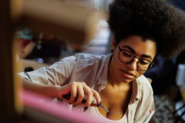 Afrika kökenli Amerikalı kadın sanatçı, resim bıçağını atölyede bulanık sehpa ve tuvalin yanında tutuyor.