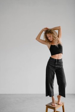 Koyu kotlu ve çıplak ayaklı kadın. Gri arka planda, taburede duruyor.