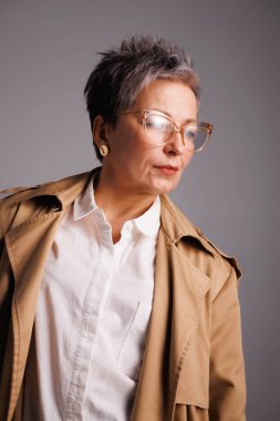 Gri renkli yağmurluk ve gözlük takmış gri saçlı zarif olgun bir kadın.