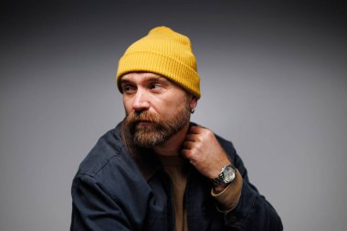 Şapkalı ve ceketli modaya uygun sakallı adam gri gömleğe dokunuyor. 