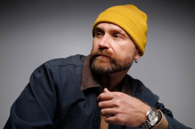 Şapkalı ve ceketli şık yetişkin bir adam. Gri üzerine izole edilmiş bir şekilde başka yere bakıyor. 