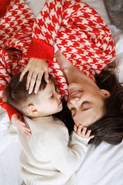 Parlak örgü elbiseli, gülümseyen bir kadının kucak dolusu kucak dolusu oğlu evde yatıyor.