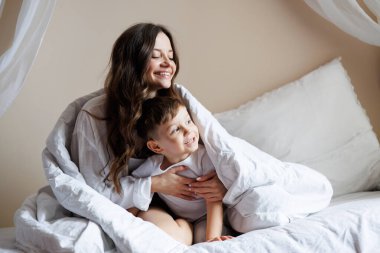 Mutlu genç bir kadın, evde battaniyenin altında bebeğe sarılıyor.