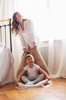 Gülümseyen anne evde küçük oğluyla oynarken halı çekiyor.