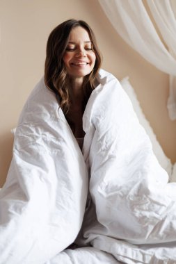 Neşeli genç esmer kadın, sabahları battaniyeye sarılıyor.