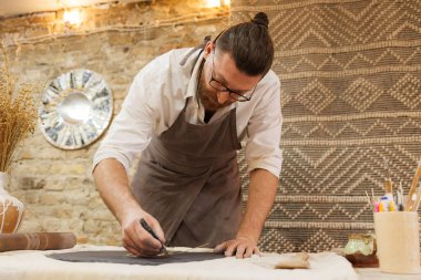 Atölyede siyah kil kesen önlüklü bir zanaatkar