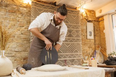 Potter, stüdyoda siyah kil ve buğday dikeninden tabak şekillendiriyor.