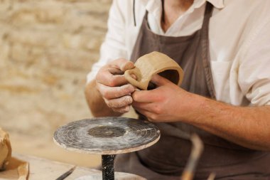 Önlükteki çömlekçiyi stüdyoda kil bardak yaparken görüntüledim.