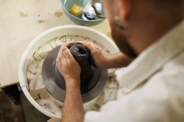 Zanaatkar stüdyoda çömlek çarkında ıslak siyah kil kalıbı döküyor.