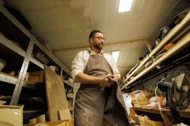 Sakallı çömlekçi atölyenin deposunda ellerini kurutuyor.