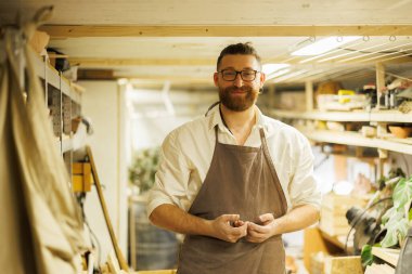 Gülümseyen çömlekçi stüdyonun bulanık deposunda kameraya bakıyor. 