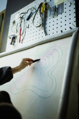 Atölyedeki aletlerin yanındaki halı tuvaline resim çizen usta kadın.