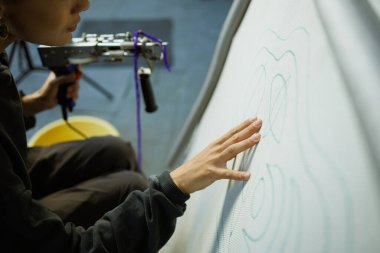 Zanaatkar kadın tuvali desenli ve elinde halı tutarak kontrol ediyor. 