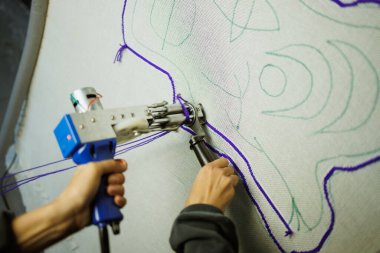 Esnaf atölyede tabancayla halı yapıyor.