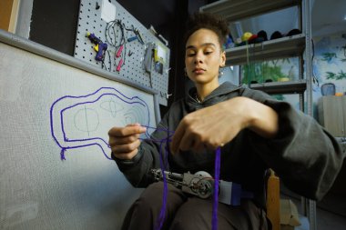 Afrikalı Amerikalı zanaatkar kadın tuval yanında iplik ve halı çekme makinesi tutuyor.