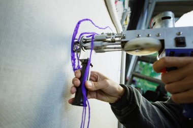 Zanaatkar kadının bir kısmı tuval tabancasıyla tuvale halı yapıyor.